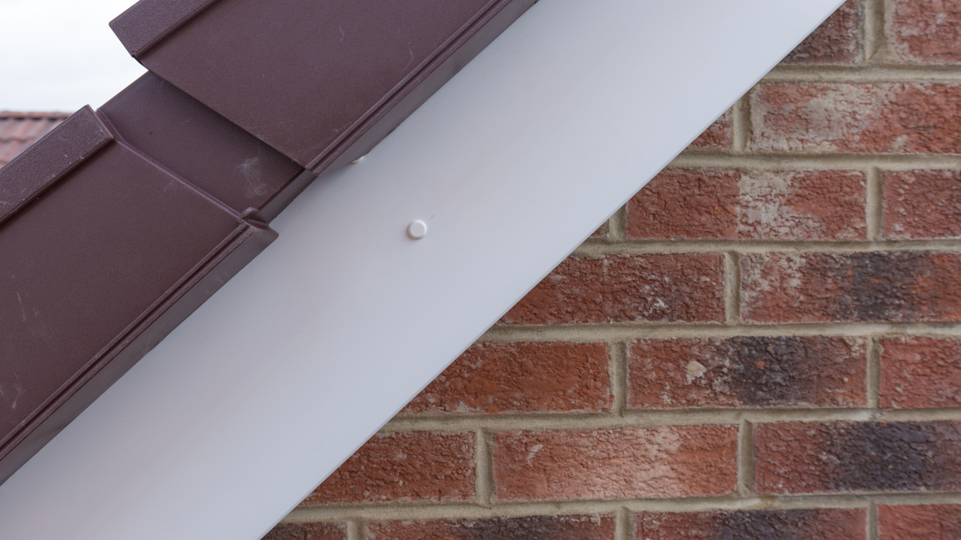 Newly fitted white soffit and brown fascia with guttering against a brick wall