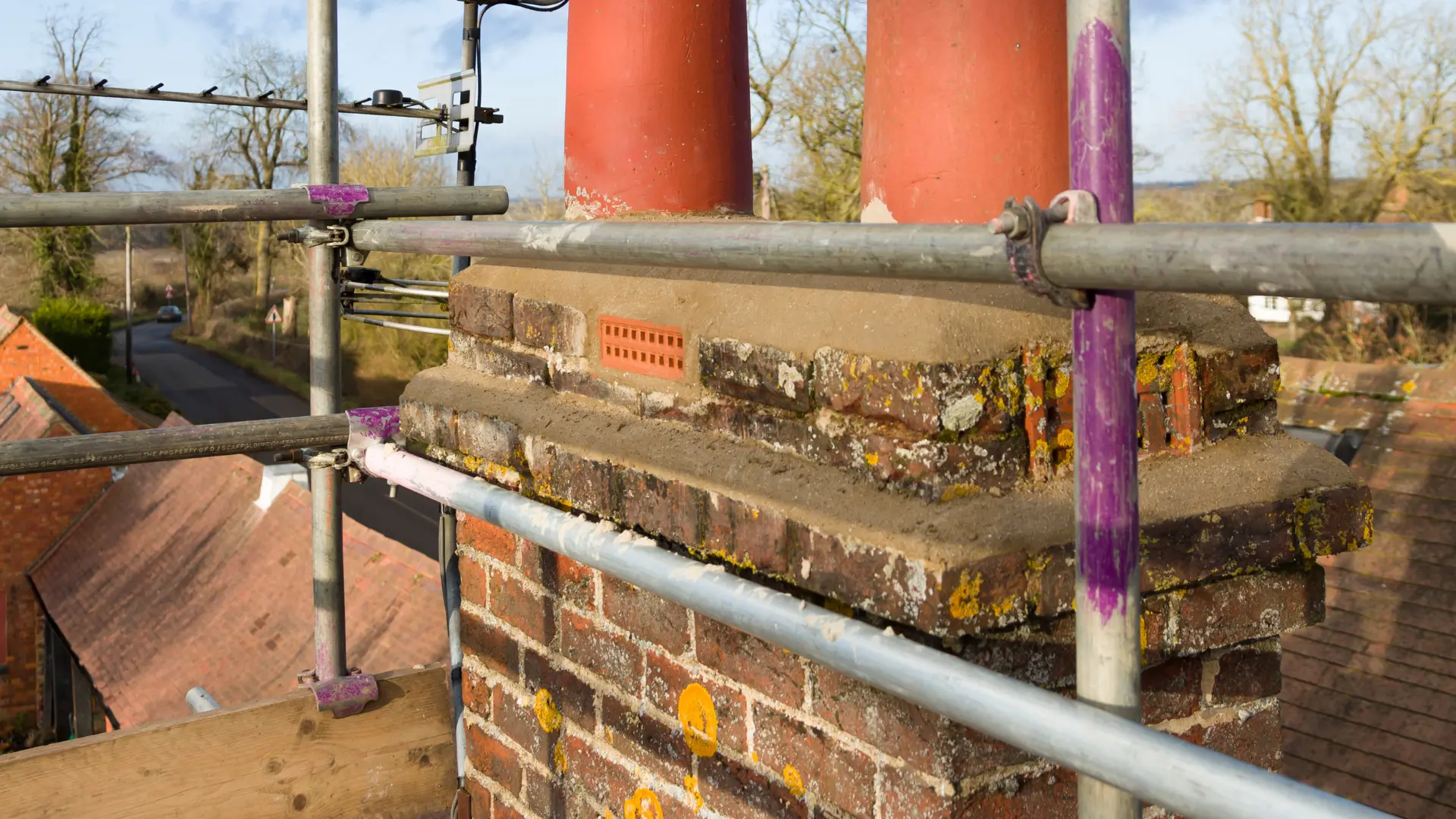 Brick chimney stack with rebuilt mortar haunching and clay pots, viewed from the scaffold