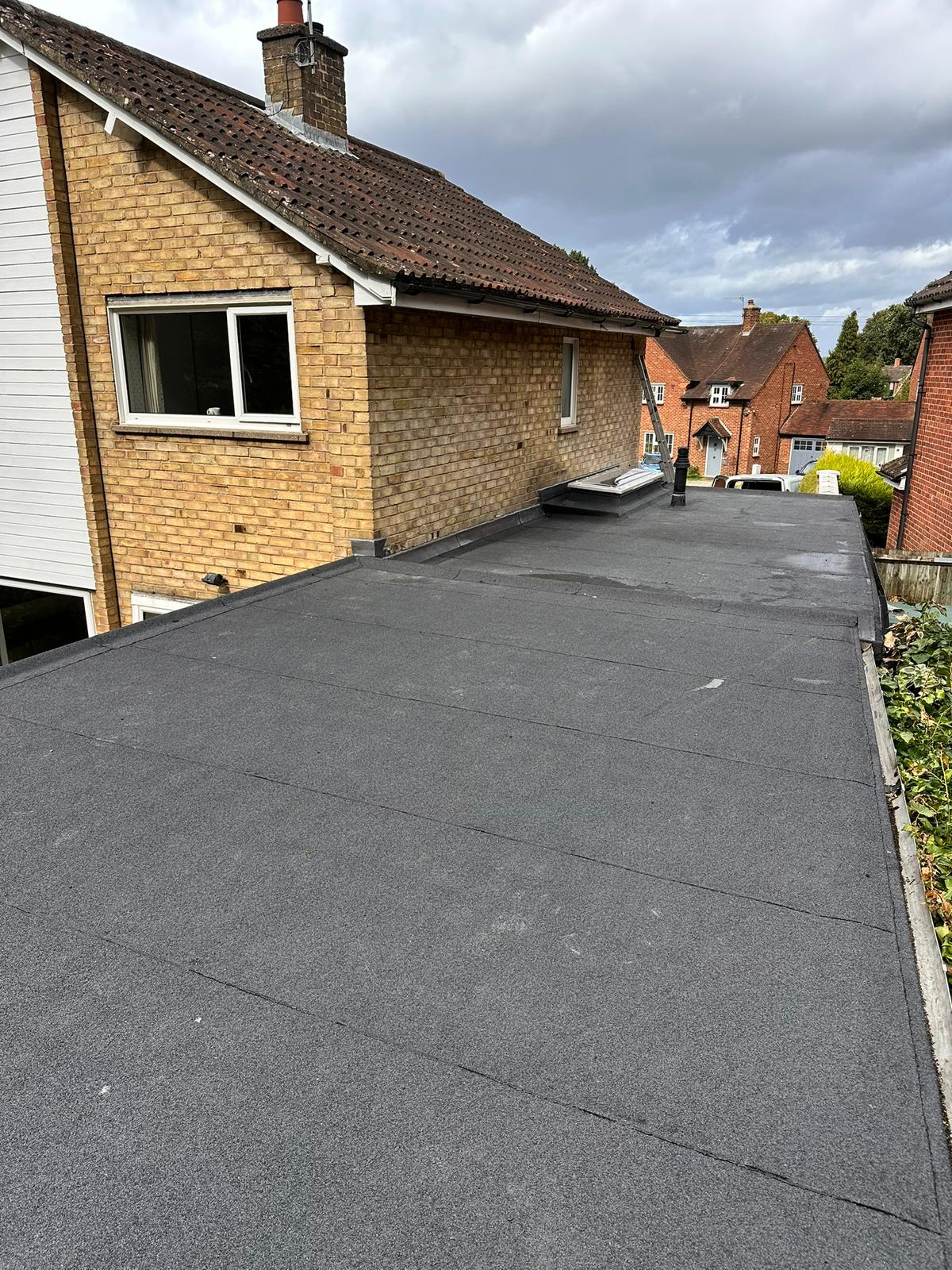 Completed flat roof covering alongside a pitched tiled roof and chimney on a brick house
